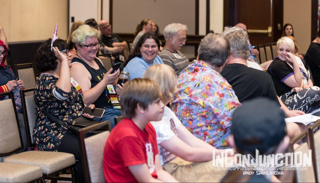 Assorted humans sitting in chairs in rows, chatting with one another