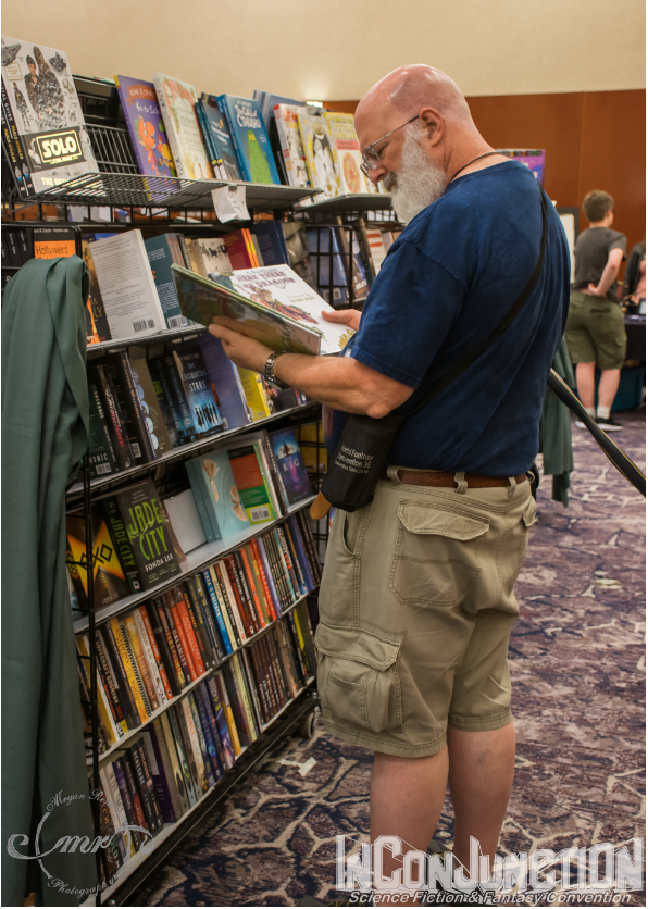 A man reading a book in front of a large rack of books for sale