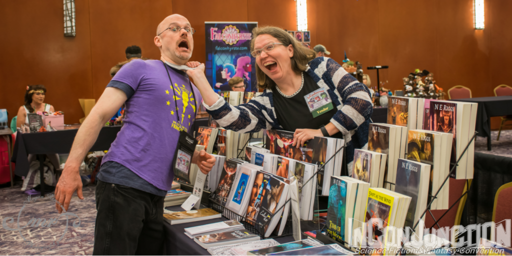 A pair of authors mock fight across a display of books on a table