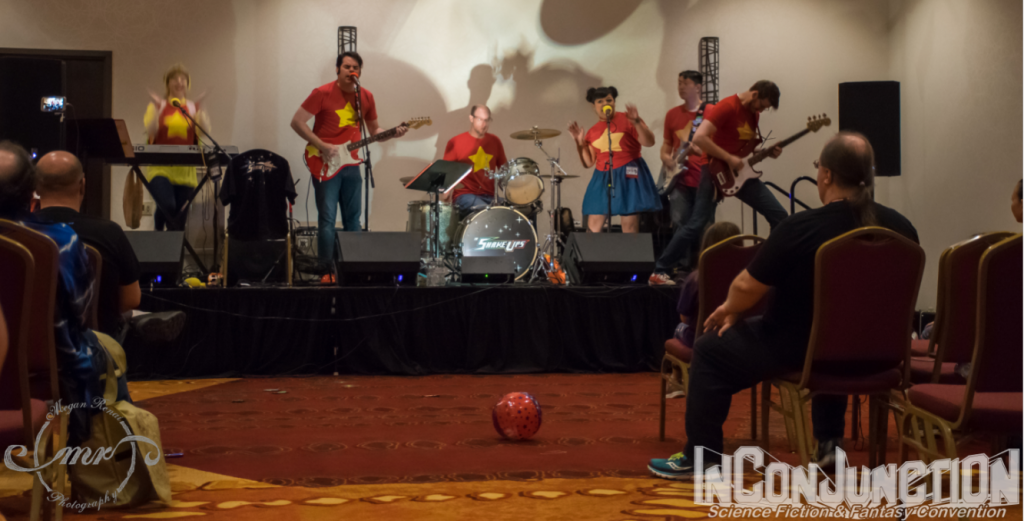 A rock band dressed in red shirts with yellow stars perform on a stage